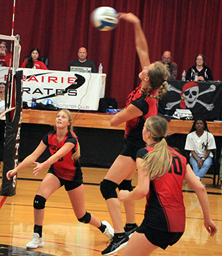 Ellie Nuxoll spikes the ball against Kamiah. Also shown are Beka Schumacher and Kylie Schumacher.