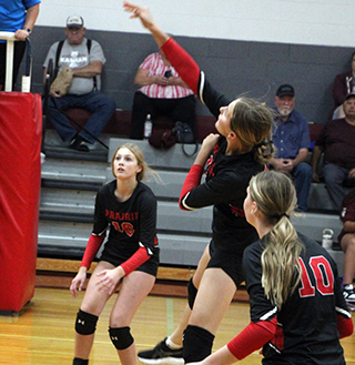 Ellie Nuxoll spikes the ball at Kamiah. Also shown are Beka Schumacher and Kylie Schumacher.