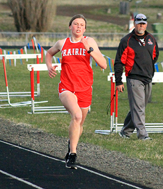 Sydney Shears comes down the final stretch to win the 1600 at the Prairie Meet as coach Ryan Hasselstrom watches.